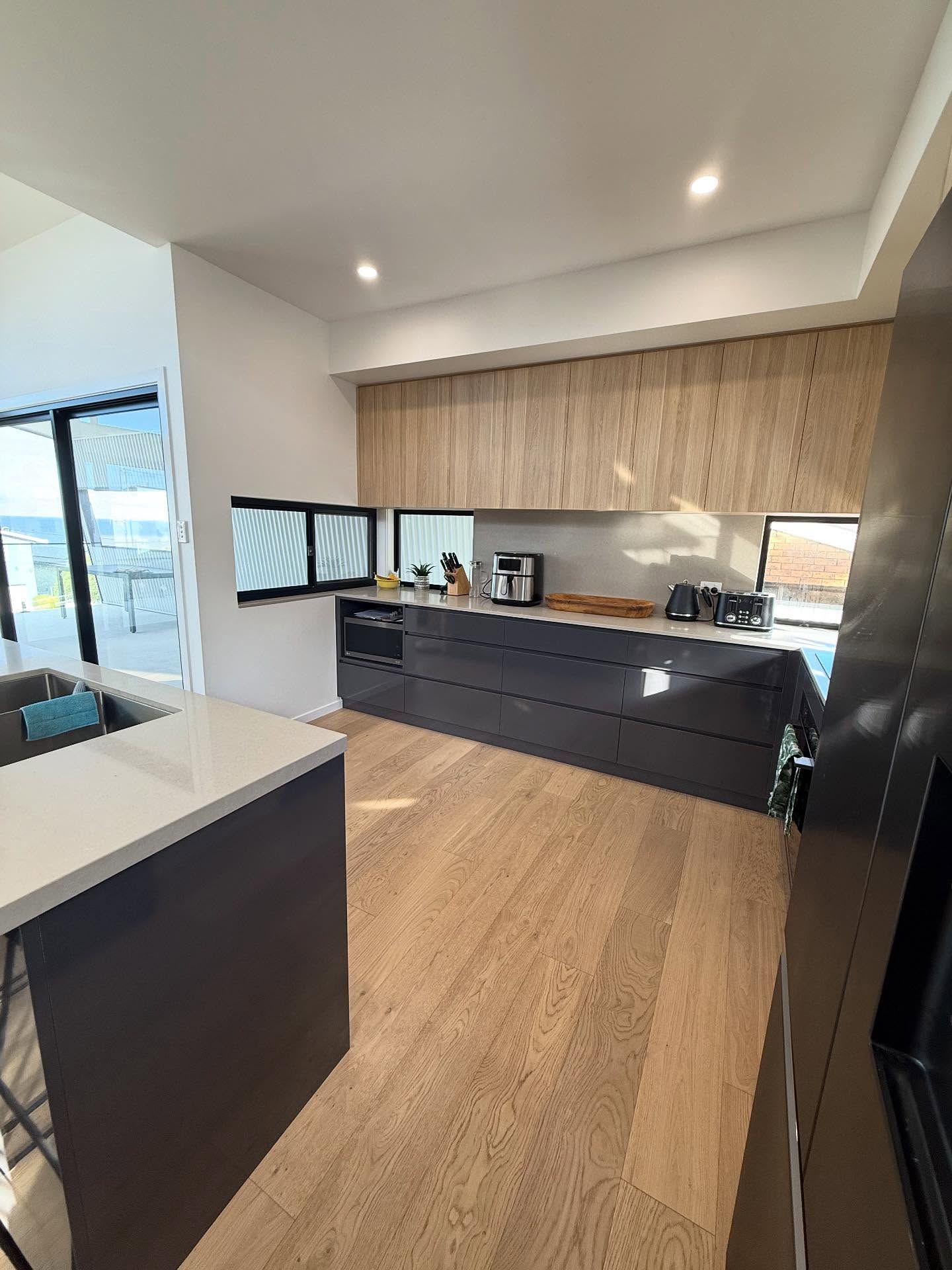 Modern kitchen with light wood floors, dark cabinets, and light wood upper cabinets  — Barrington Coast Homes in Tallwoods, NSW