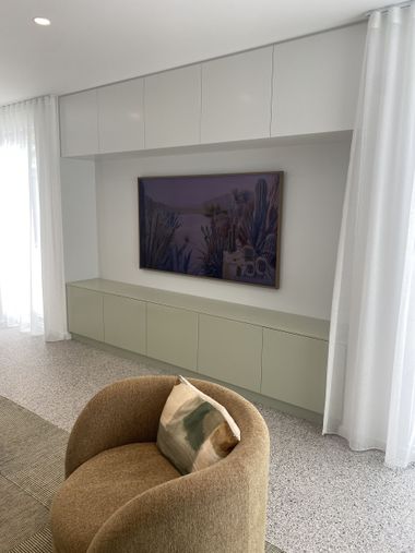 Living room with built-in storage, a TV, and a cozy chair. Neutral tones with a colorful landscape art.