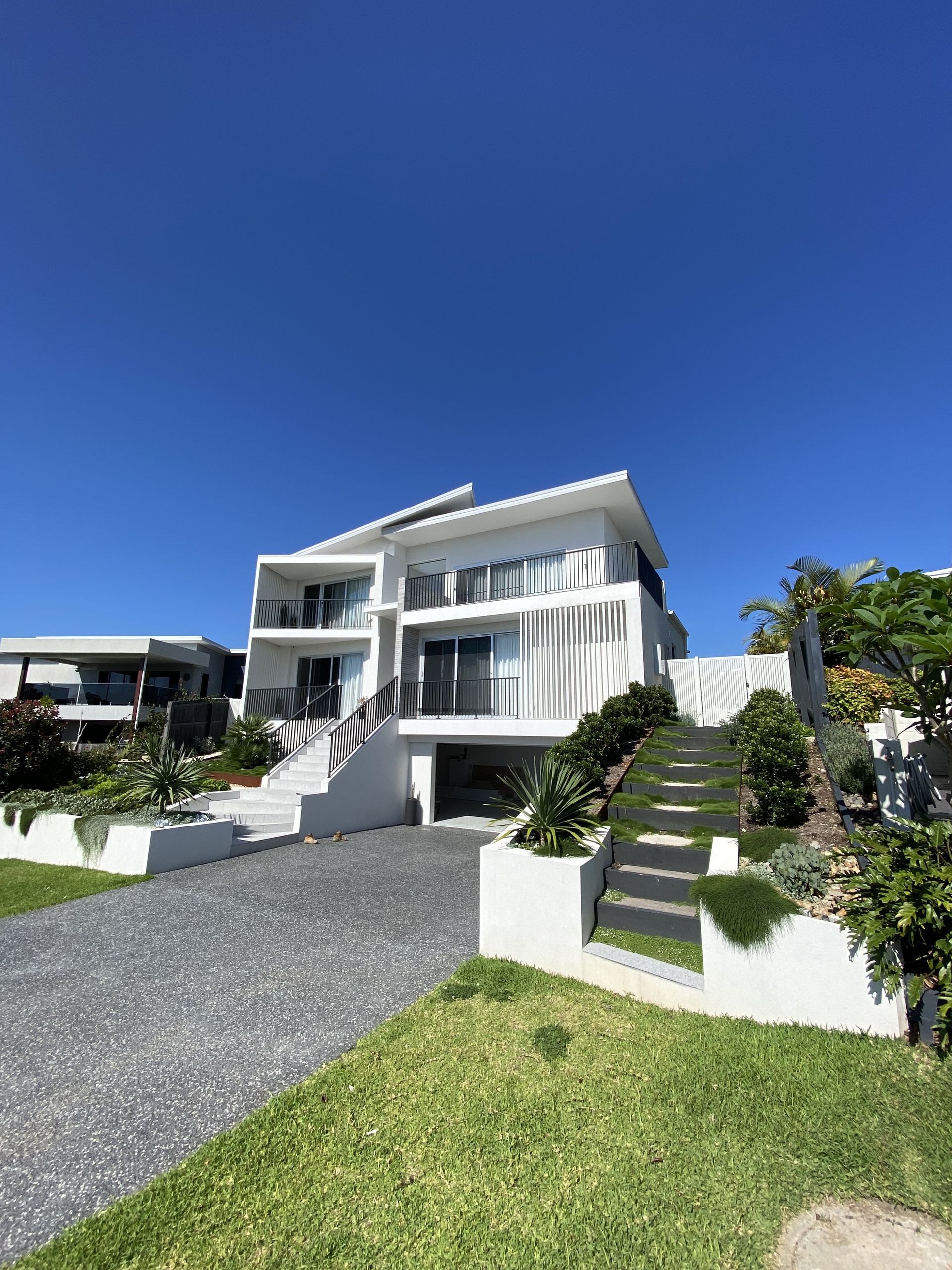 White modern house with a gray gravel driveway under a clear blue sky. — Barrington Coast Homes in Tallwoods, NSW