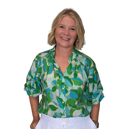 A woman wearing a green and blue shirt and white shorts is smiling.