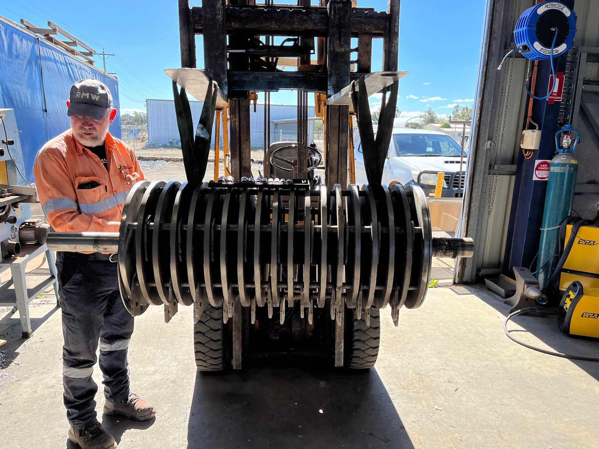 A man is standing in front of a forklift holding a large piece of metal.