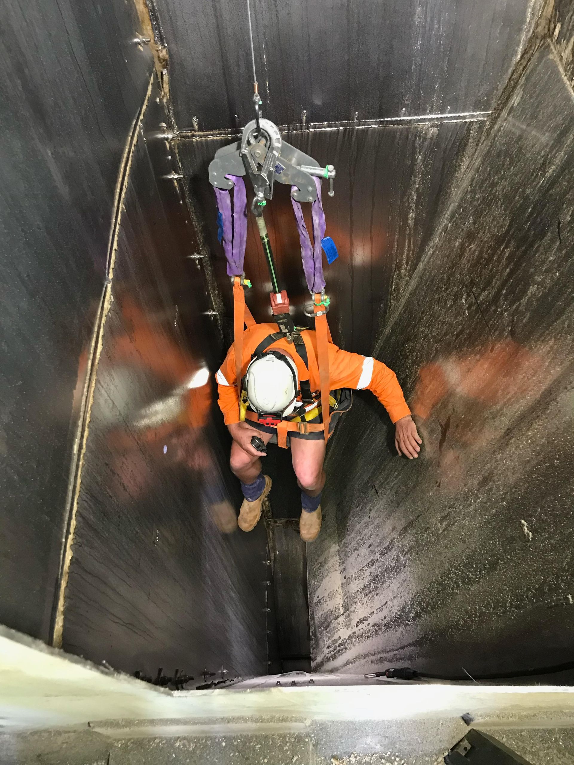 Man wearing a harness repairing a feed mill at height.