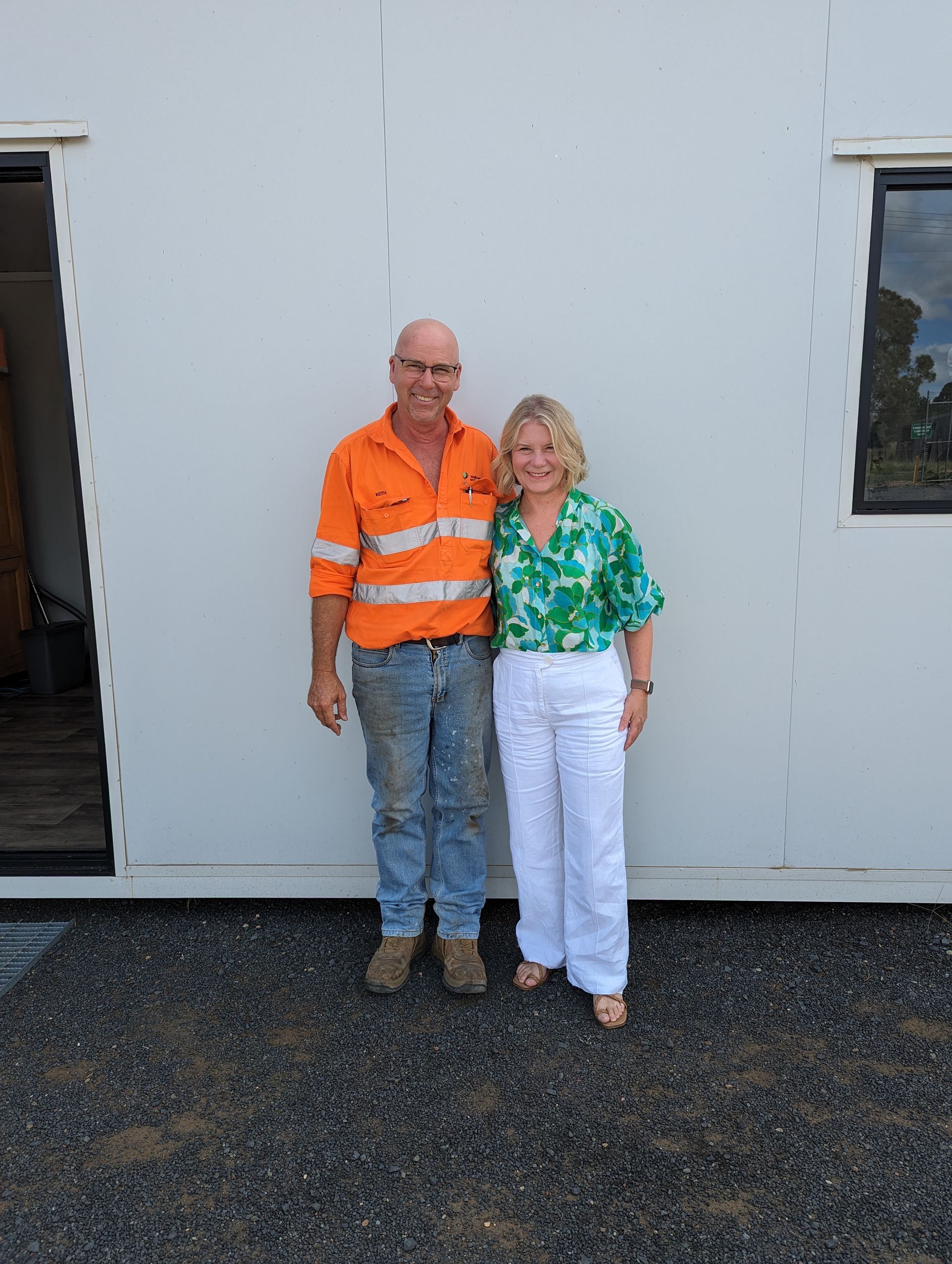 A man and a woman are standing in front of a white building.