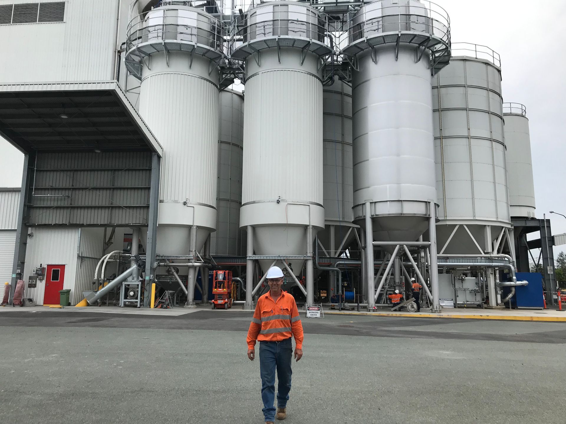 A man in a hard hat is standing in front of large silos
