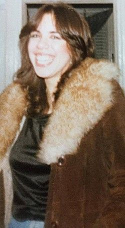 A woman is wearing a fur coat and smiling.