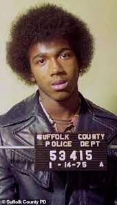 A man with an afro is wearing a leather jacket and a mug shot.