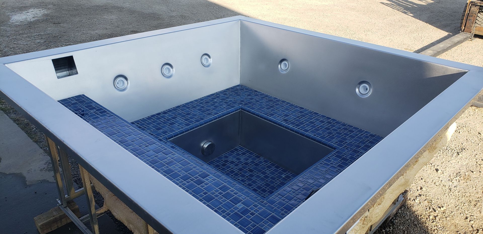 Square stainless steel hot tub with blue tiled seating and jets.