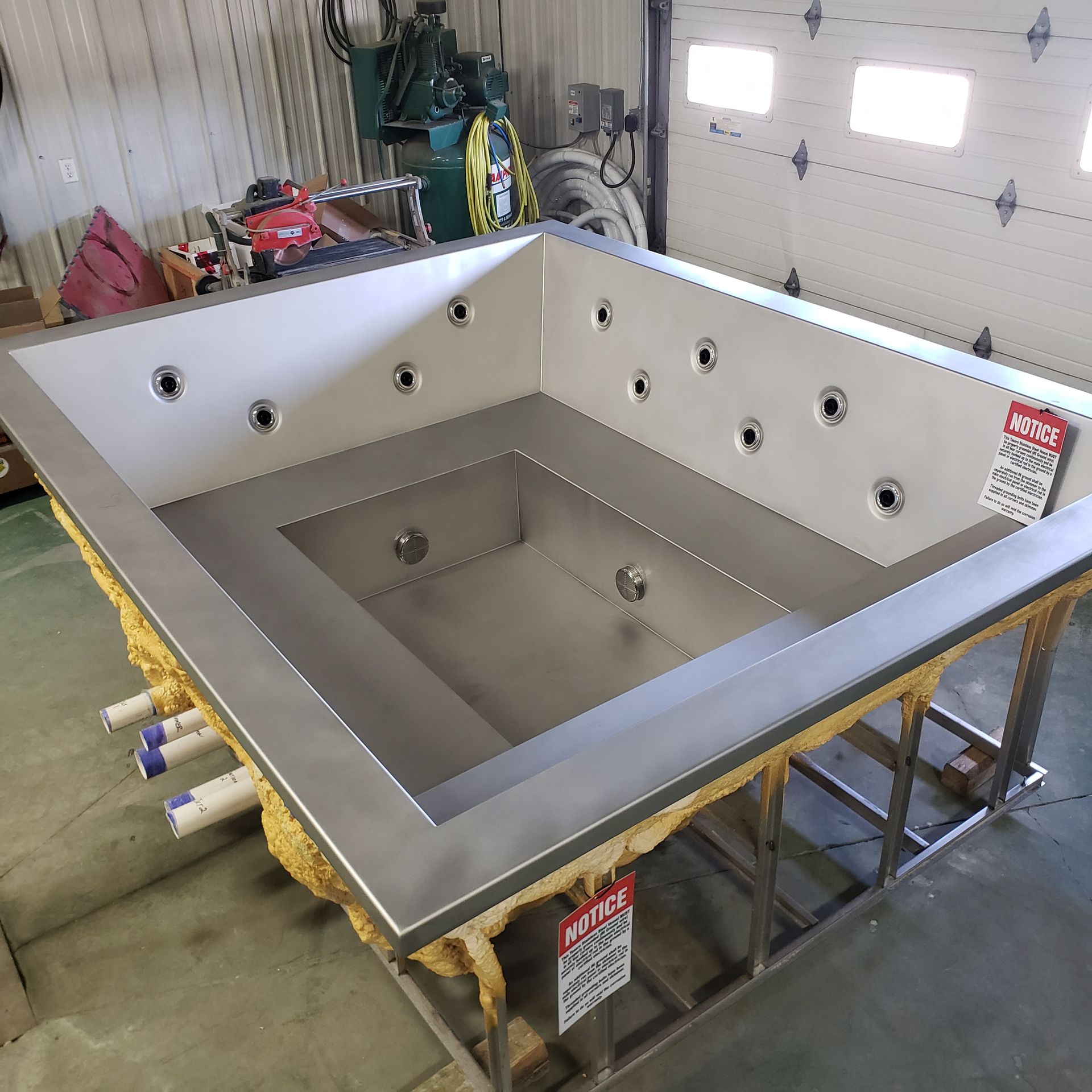 Stainless steel jacuzzi tub under construction, with jets, steps, and insulation.