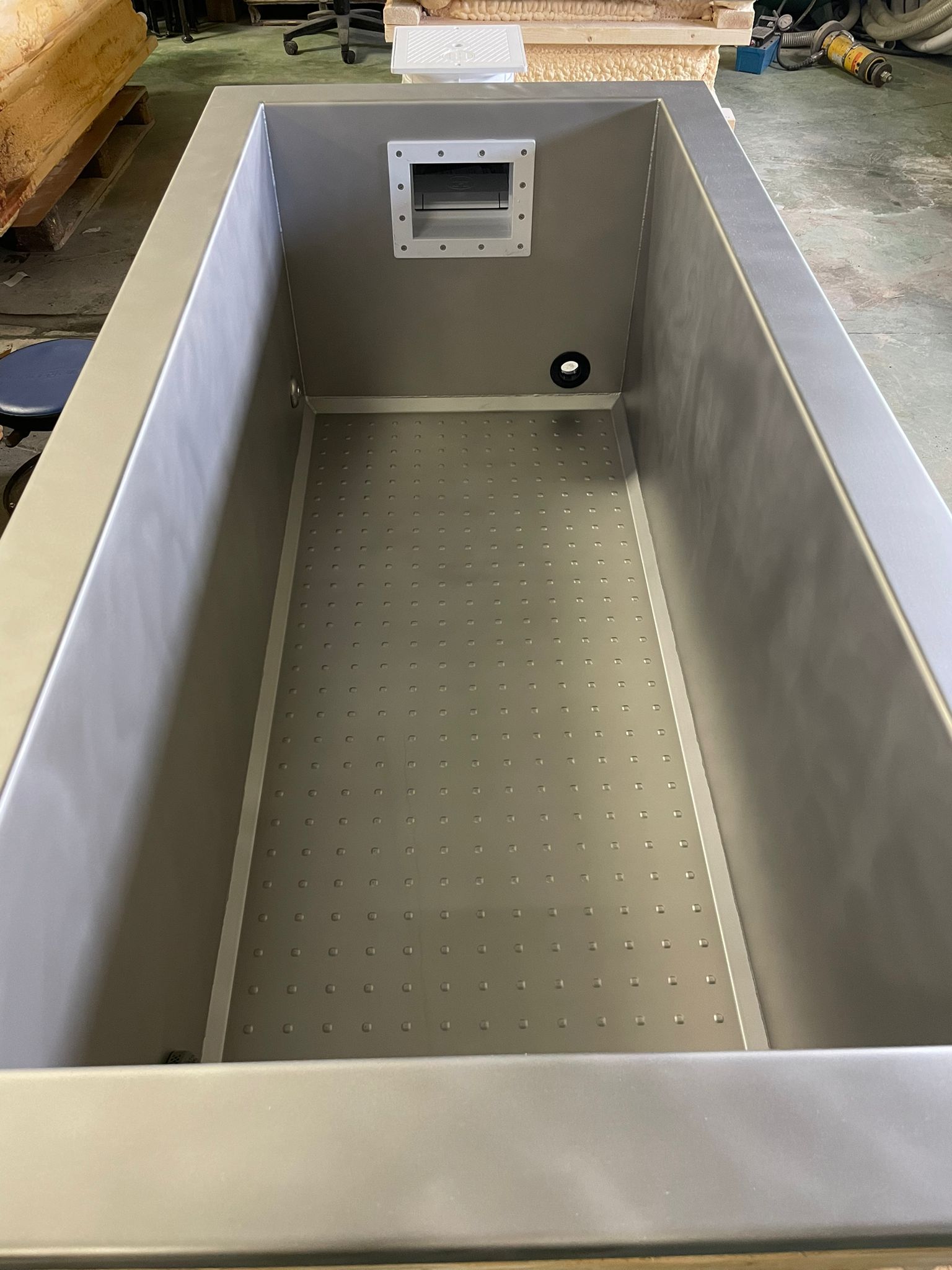 Stainless steel rectangular tank with a perforated bottom and a rectangular opening on one end.