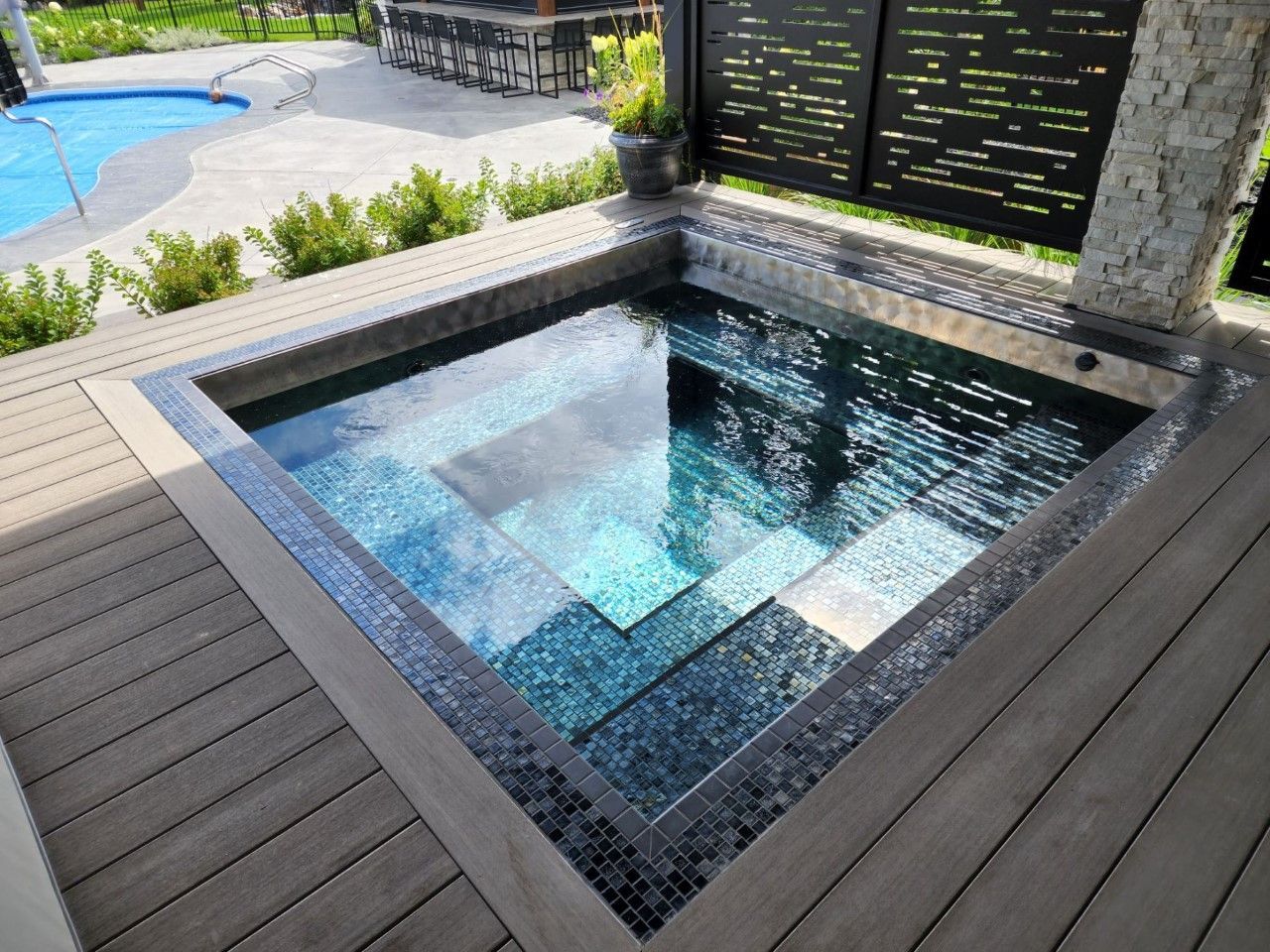 Small, square plunge pool with steps, surrounded by wooden deck. Dark blue-green tiled interior.