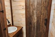 Small rustic bathroom with wood-paneled walls, white tile, a sink, and a wooden shower door
