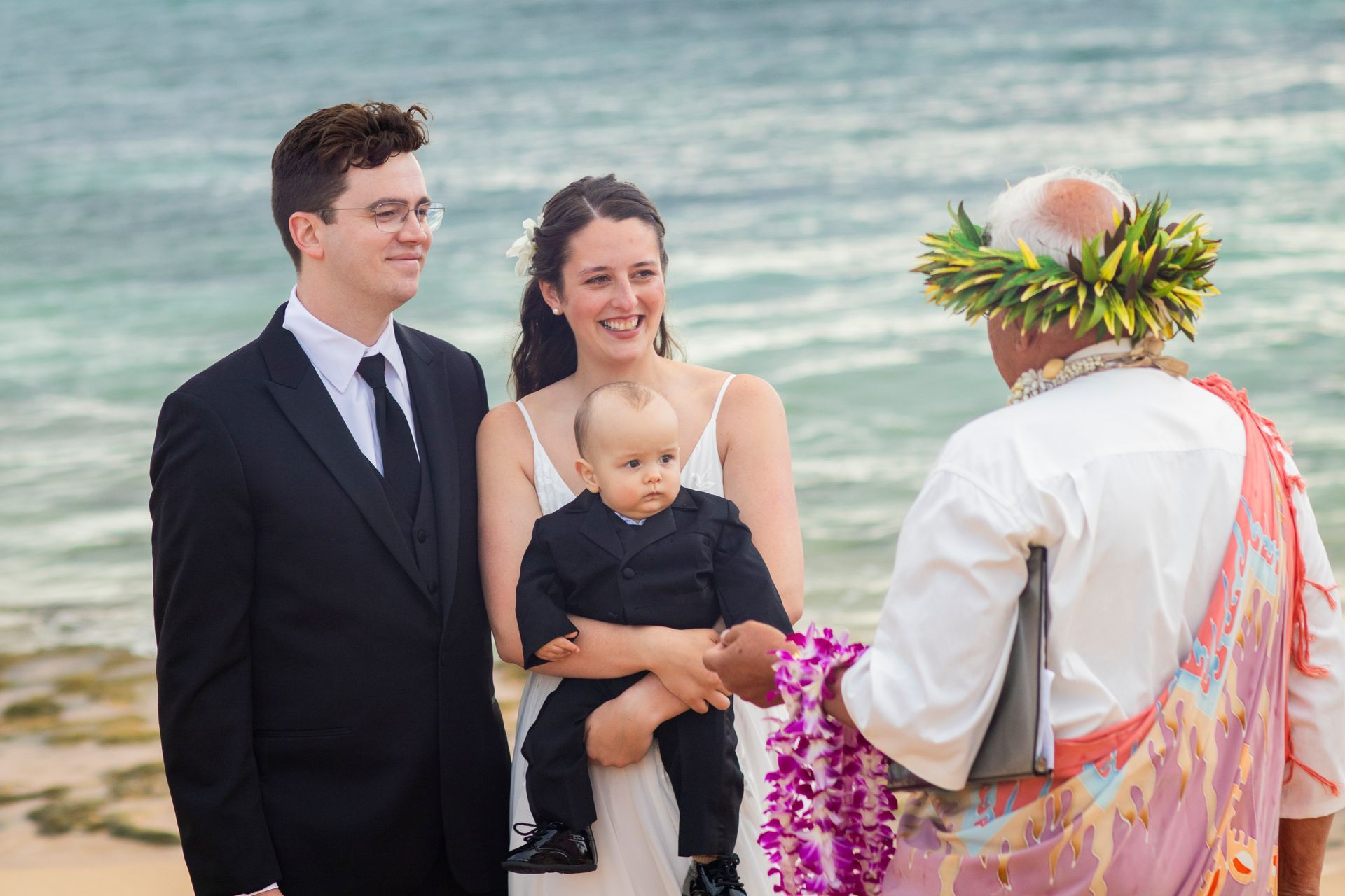Wedding on the beach with officiant, couple, and child; ocean in background.
