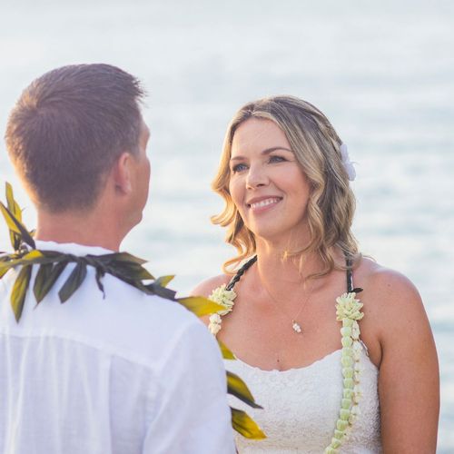 Couple exchanging vows outdoors; woman in white dress smiles, man in white shirt.