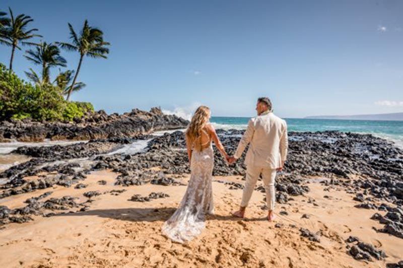 couple holding hands looking out at water on beach