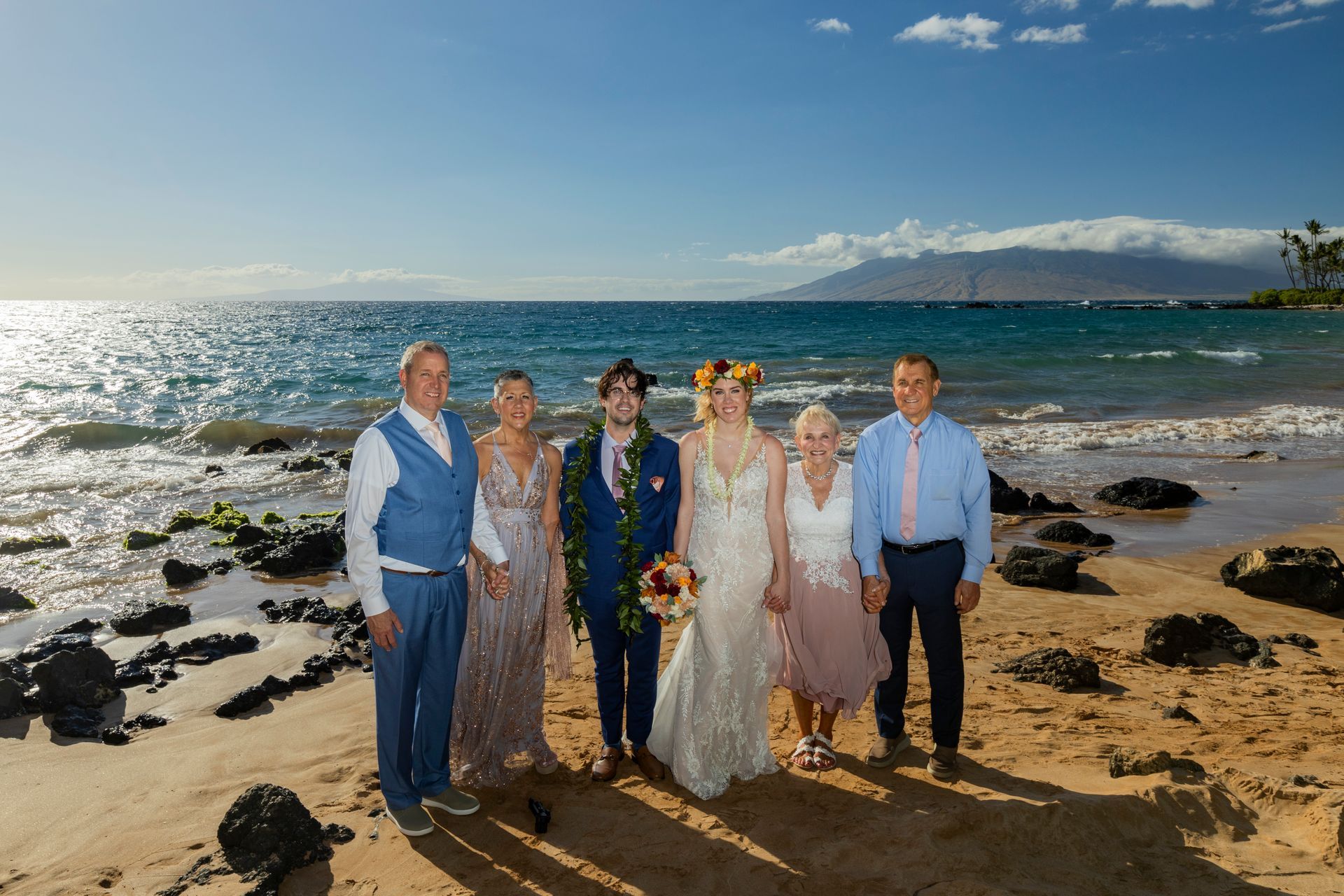 Wedding party on a beach in front of the ocean. Bride and groom with their parents posing in sunlight.