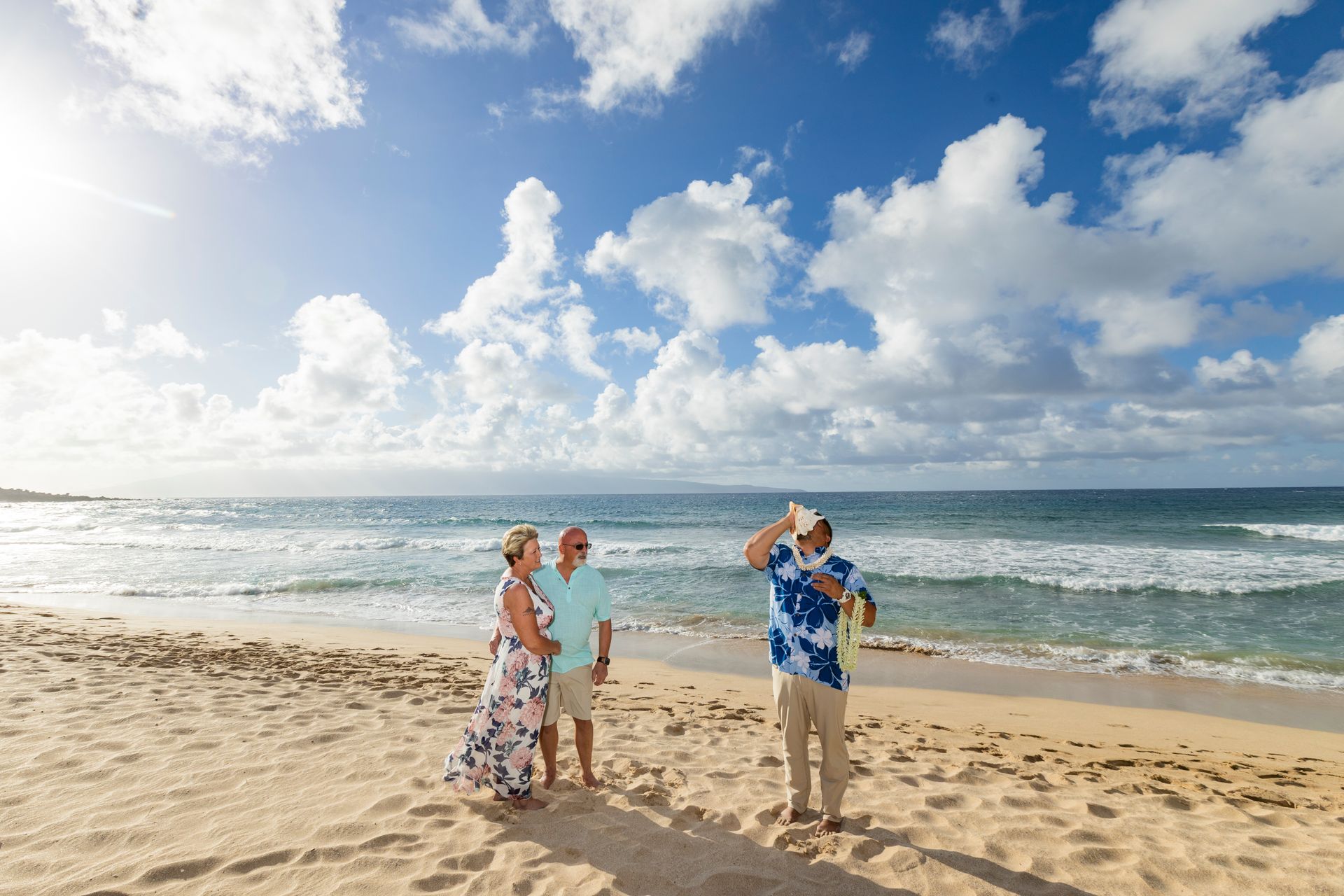 Couple on beach watches man take a photo, sunny day with blue sky and ocean.