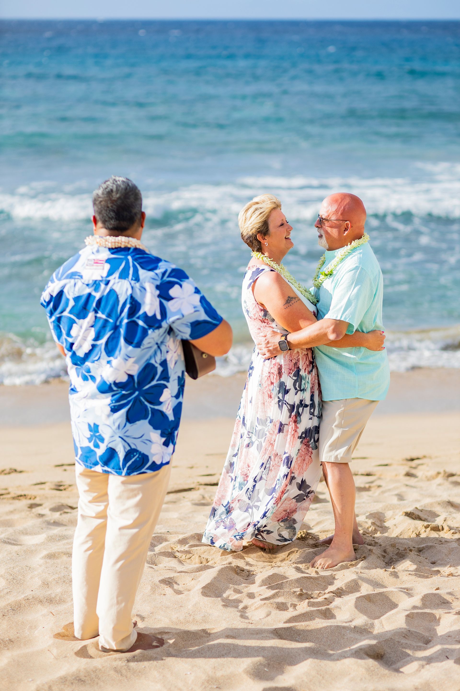 Wedding on a beach: couple embracing, man in floral shirt plays guitar, blue ocean.