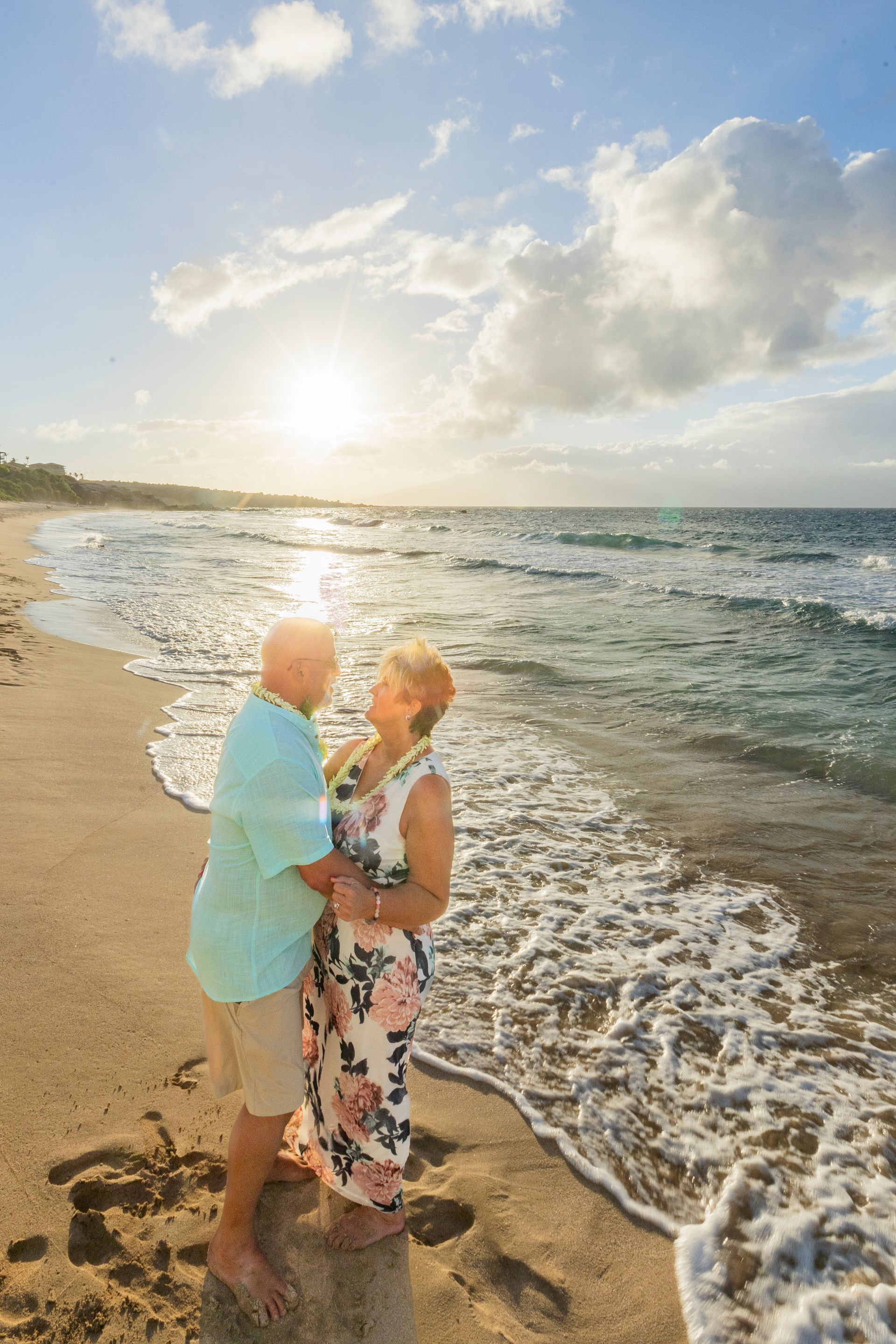 Couple embraces on a beach at sunset; ocean waves gently crash.