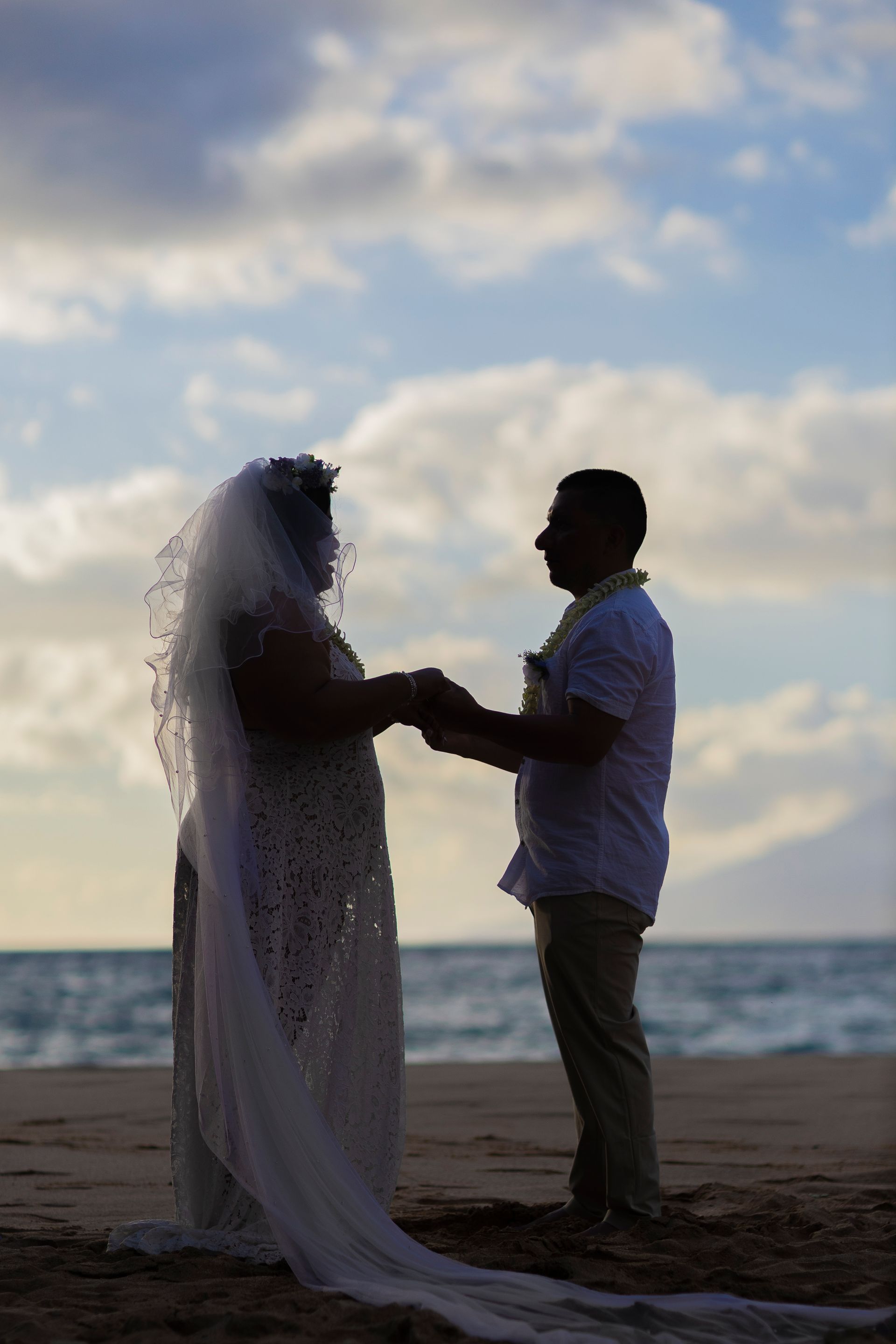 Couple holding hands on a beach, silhouetted against a sunset sky and ocean.