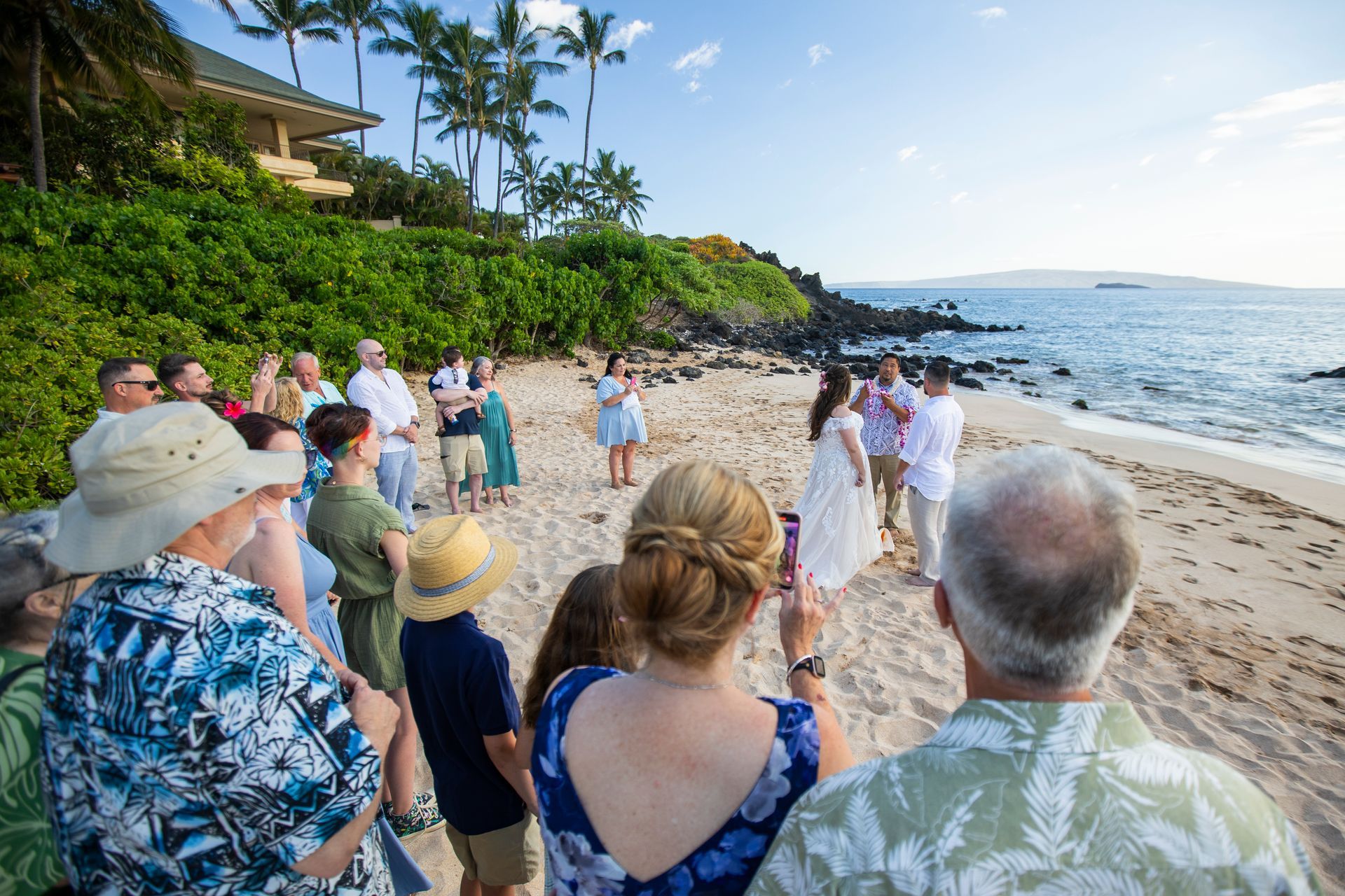 Wedding ceremony on a beach; bride and groom in front of guests, ocean in background.