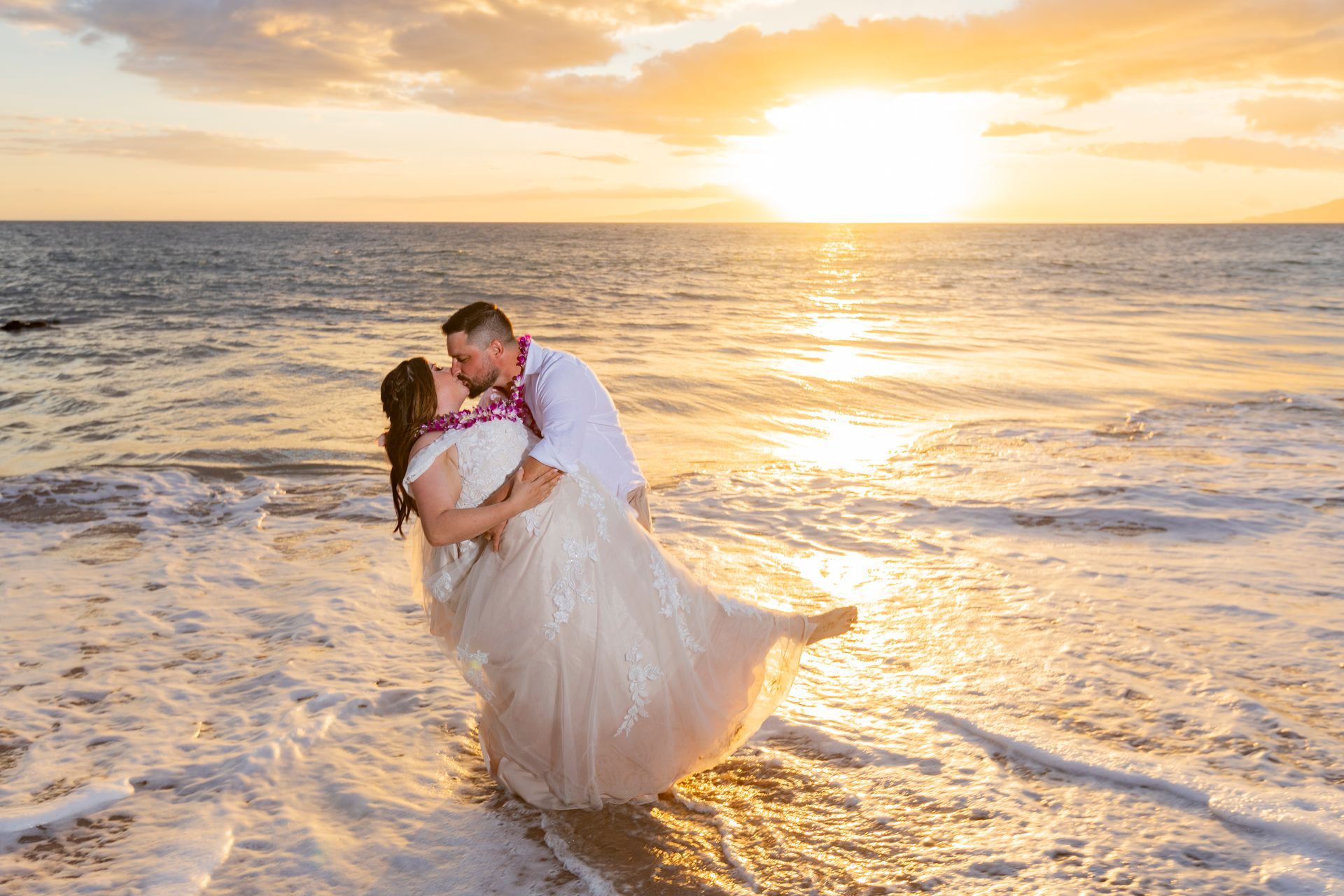 Couple kissing in the ocean at sunset. The man lifts the woman as waves crash around them.