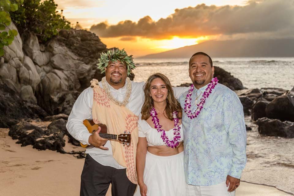 Wedding couple with musician on beach at sunset.