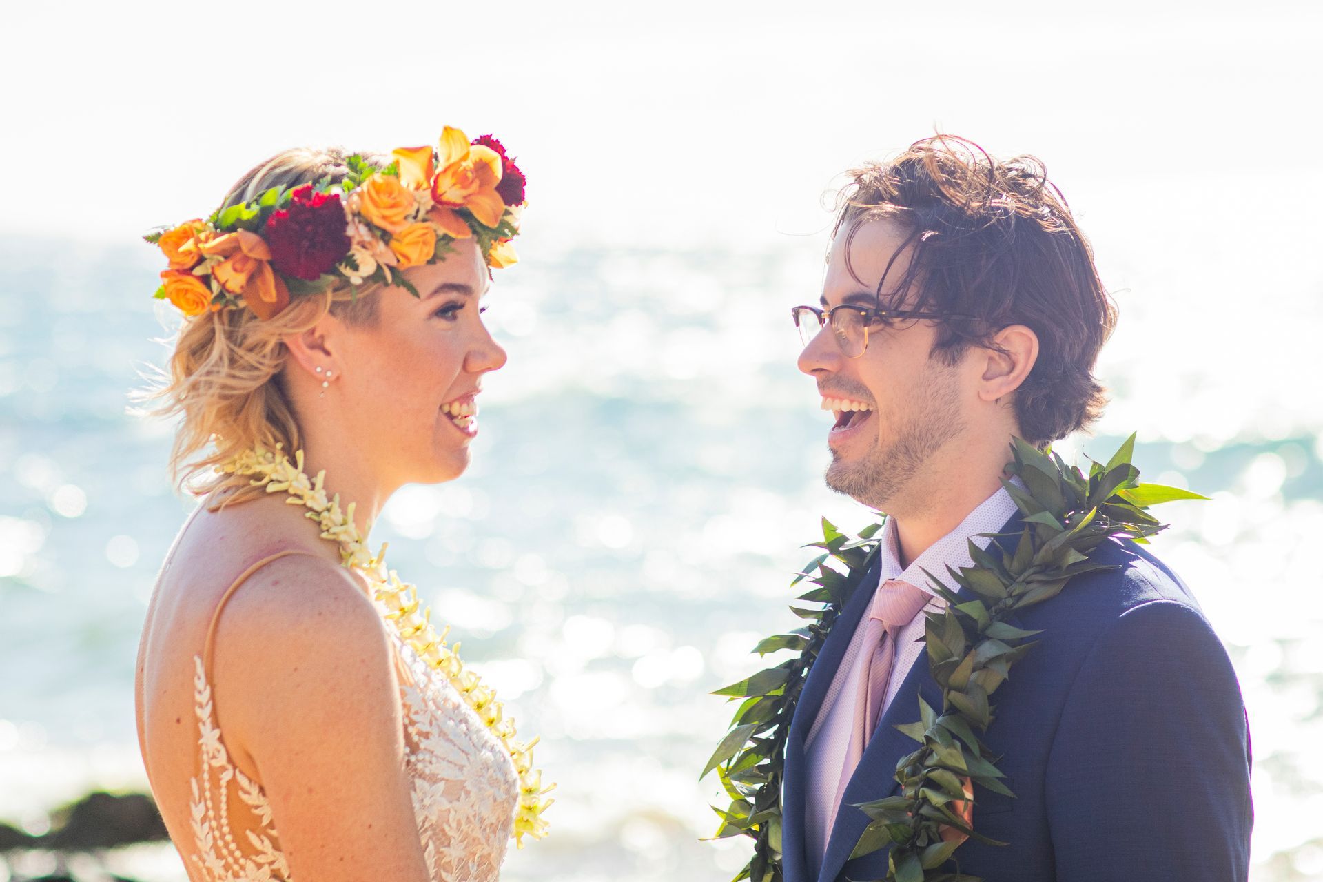 Bride and groom laughing at a beach wedding, bride wearing flower crown, groom in blue suit.