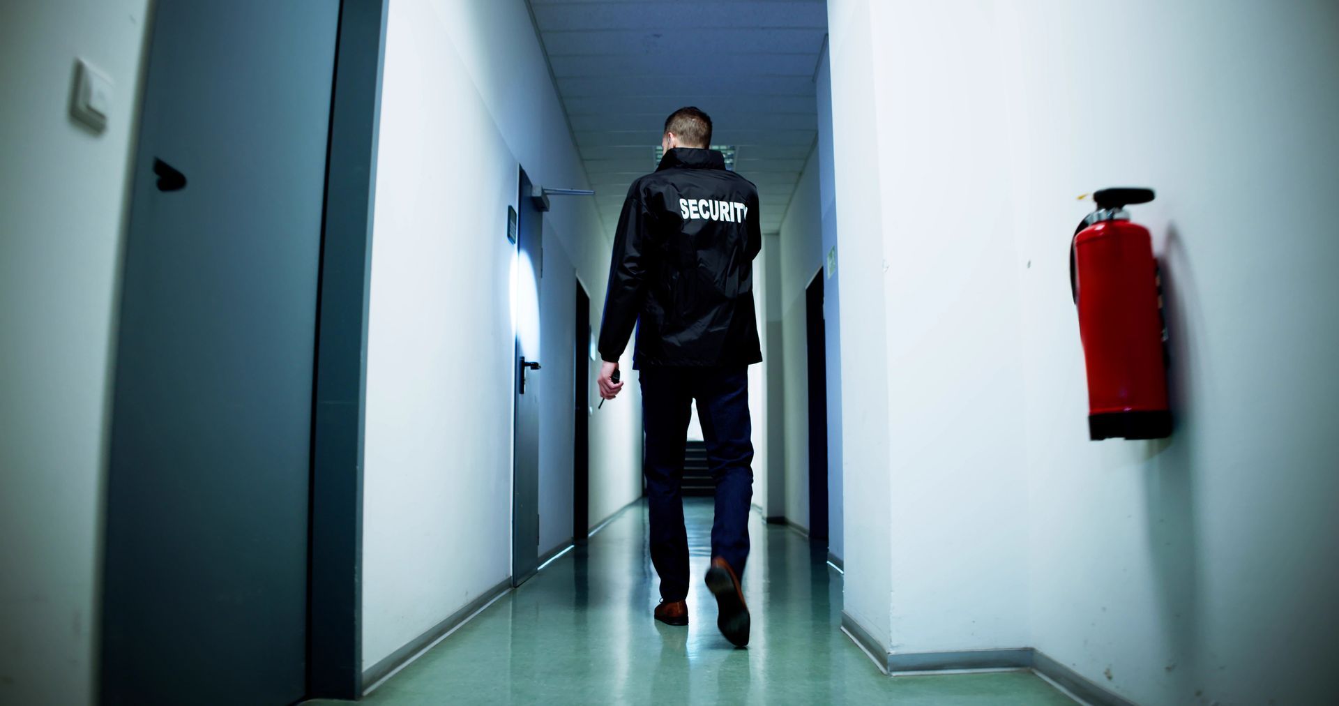 Man walking down a hallway, wearing a black jacket with 