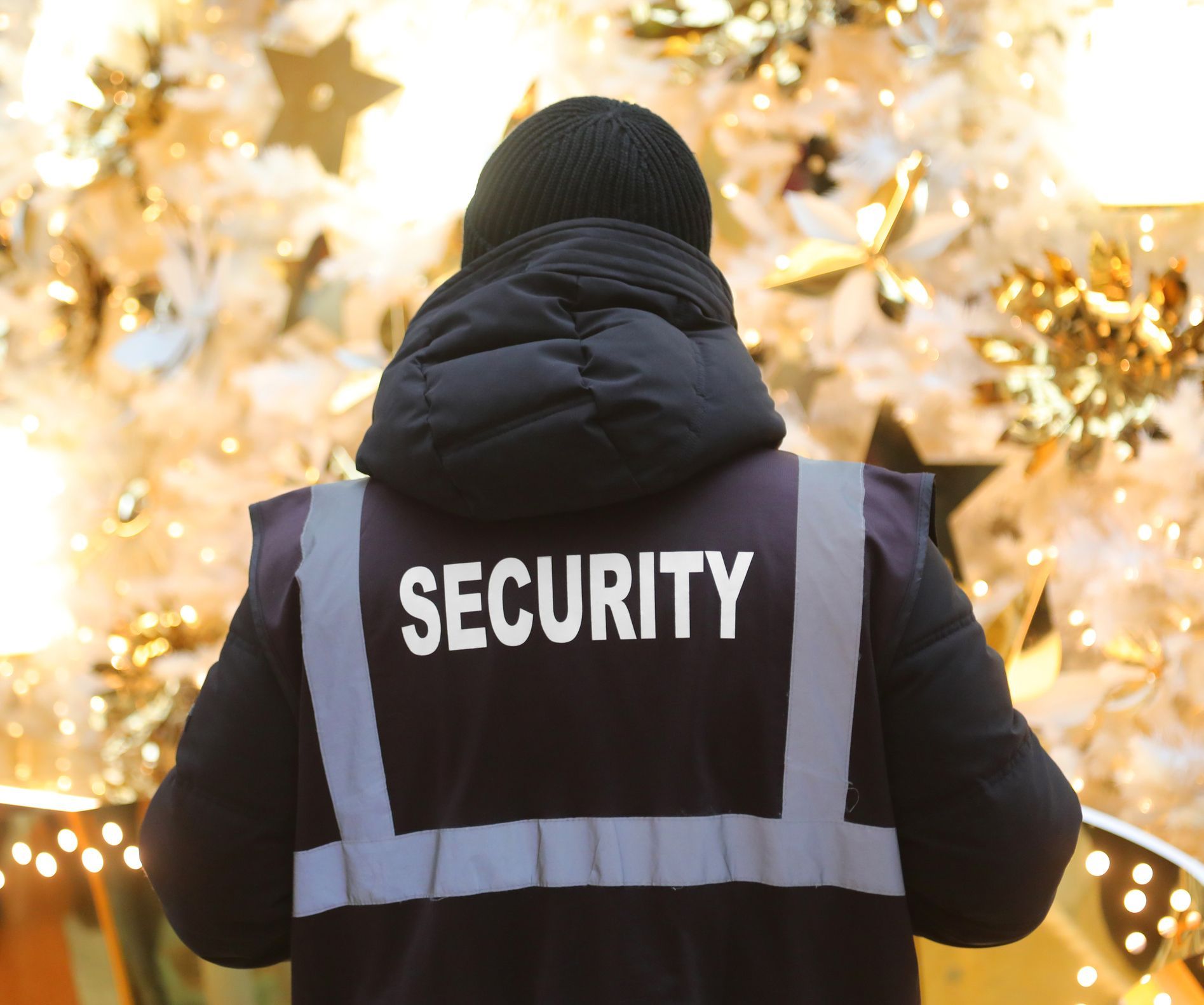 Security guard in black jacket with reflective vest, standing in front of holiday decorations.