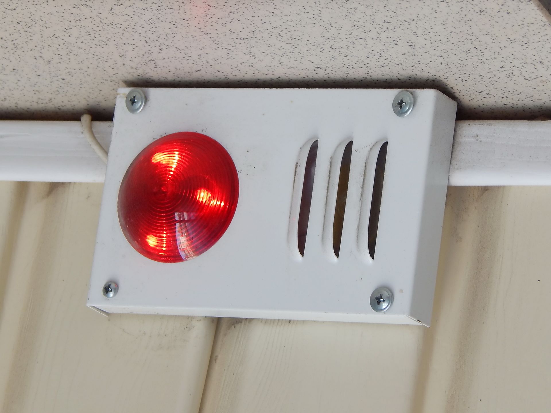 White box with red light and three vertical slits, mounted on a ceiling above a curtain.