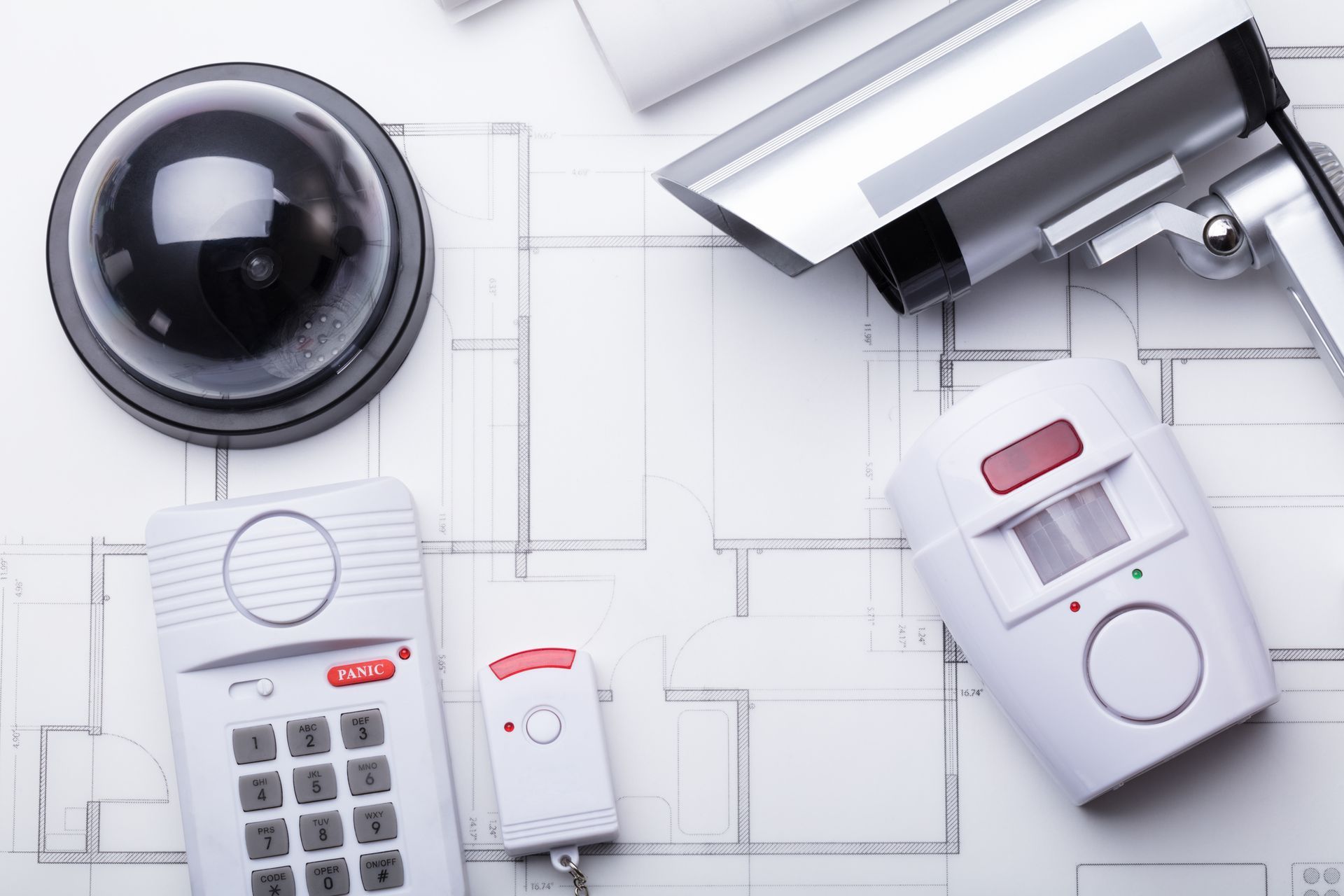 Security equipment on a blueprint: dome camera, surveillance camera, keypad, remote, and motion sensor.