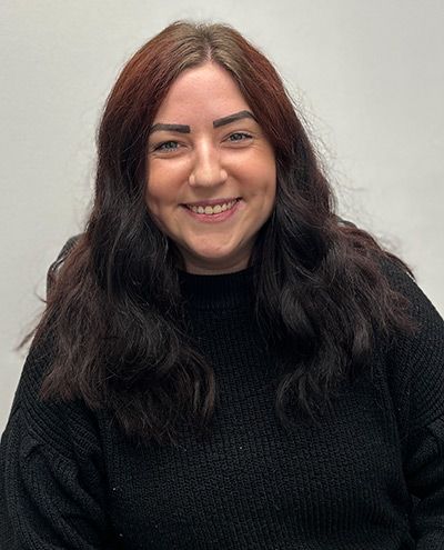 Woman with dark wavy hair smiles at the camera, wearing a black sweater.
