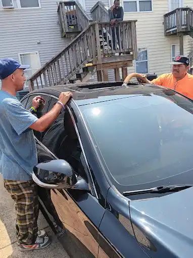 Two men are working on a car in front of a house.