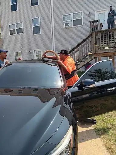 A man is standing next to a black car in front of a house.