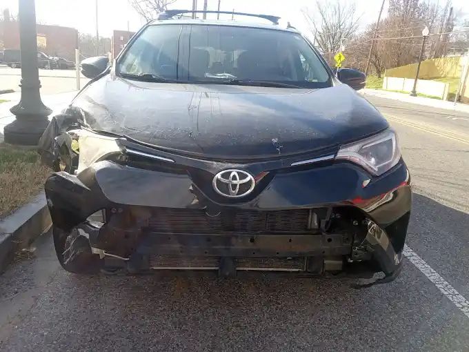 A black toyota rav4 with a damaged front bumper is parked on the side of the road.