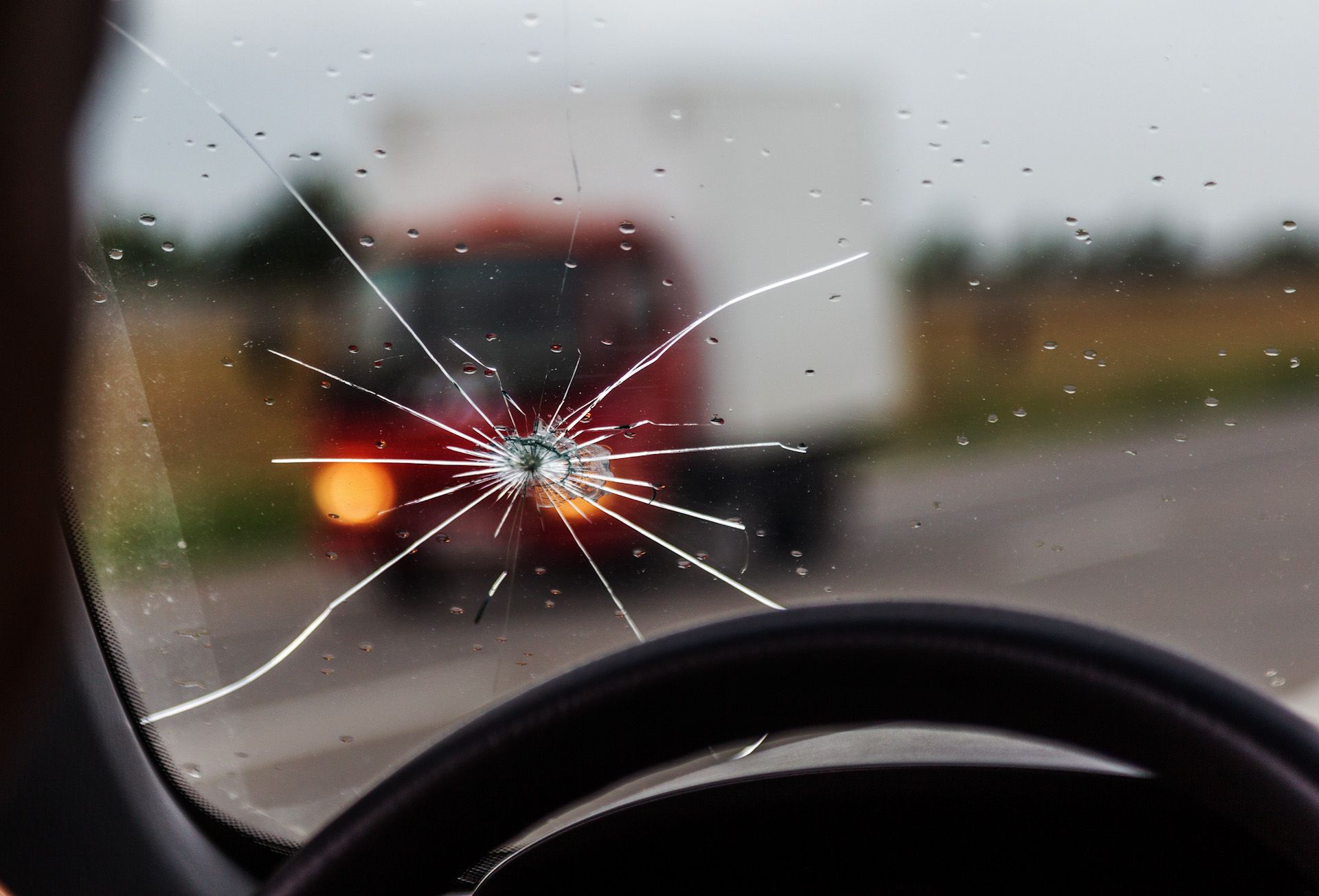 A broken windshield of a car with a truck in the background.