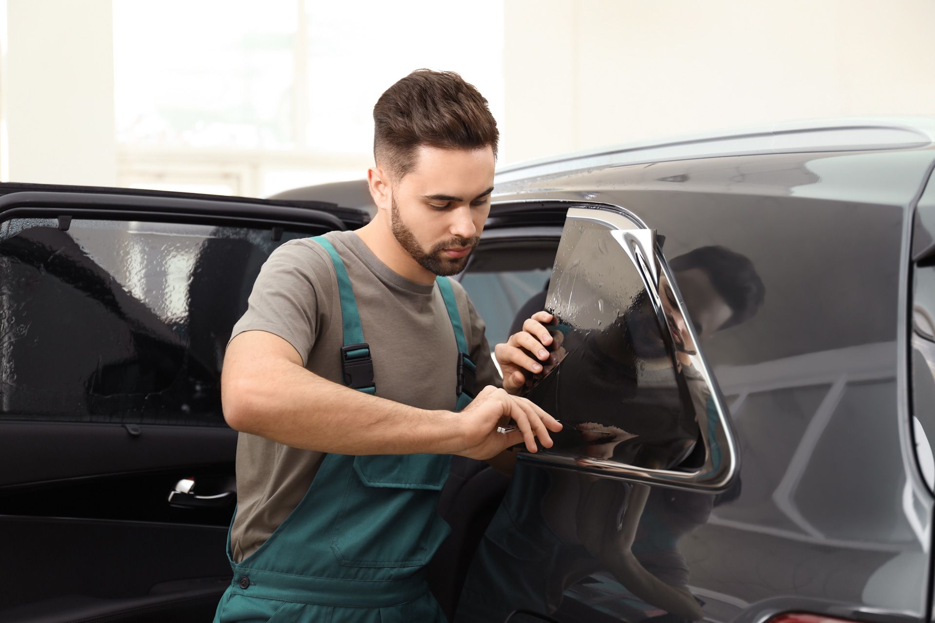 A man is applying tinted glass to a car window.