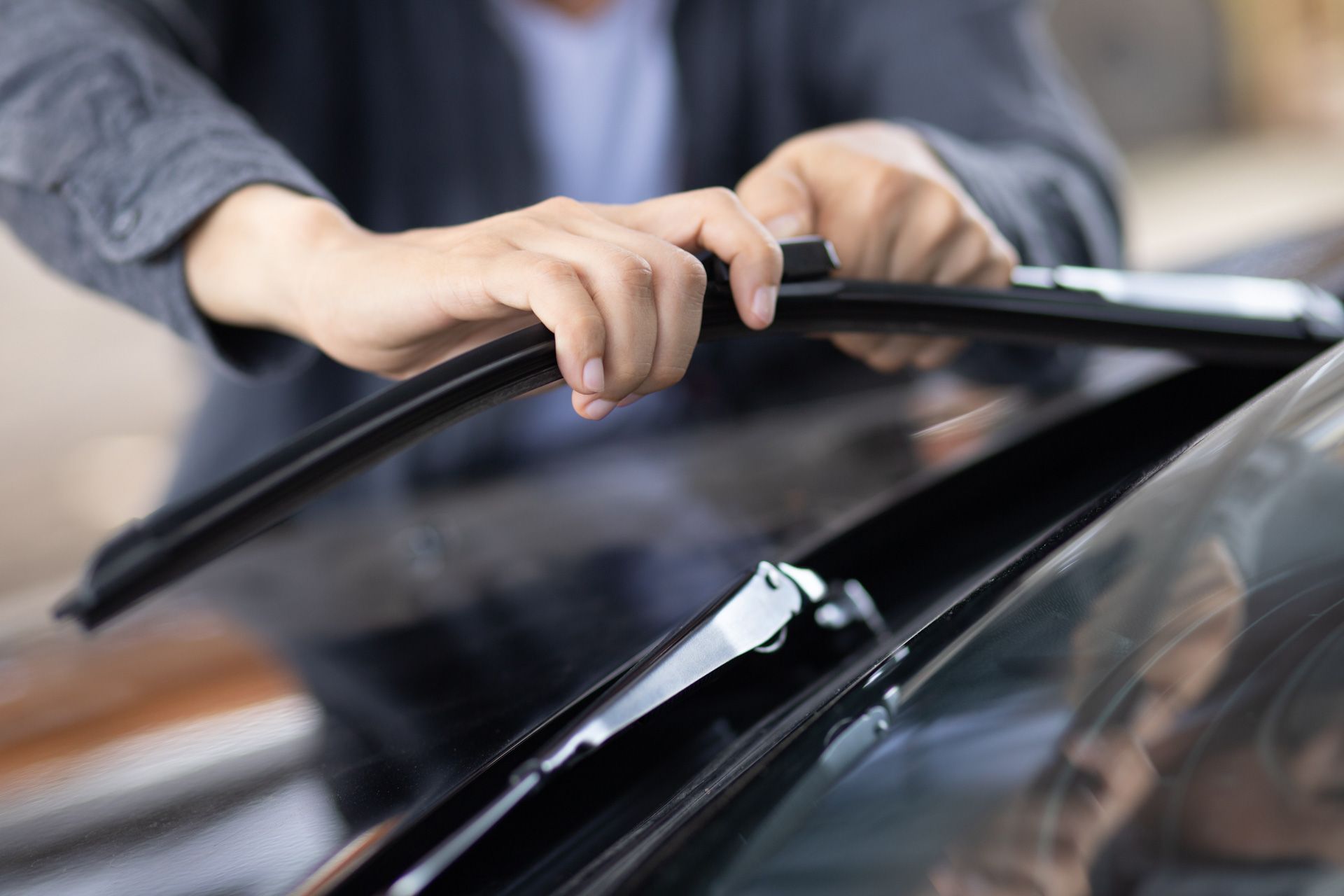 A man is cleaning the windshield of a car with a wiper blade.