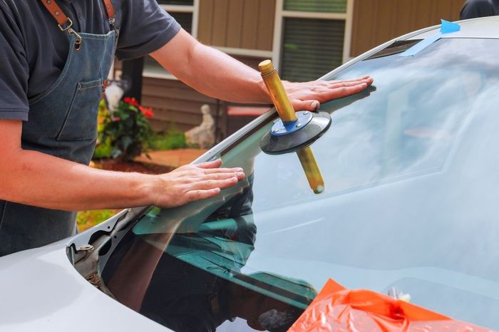 Person repairing a car windshield with a suction tool and hands on the glass