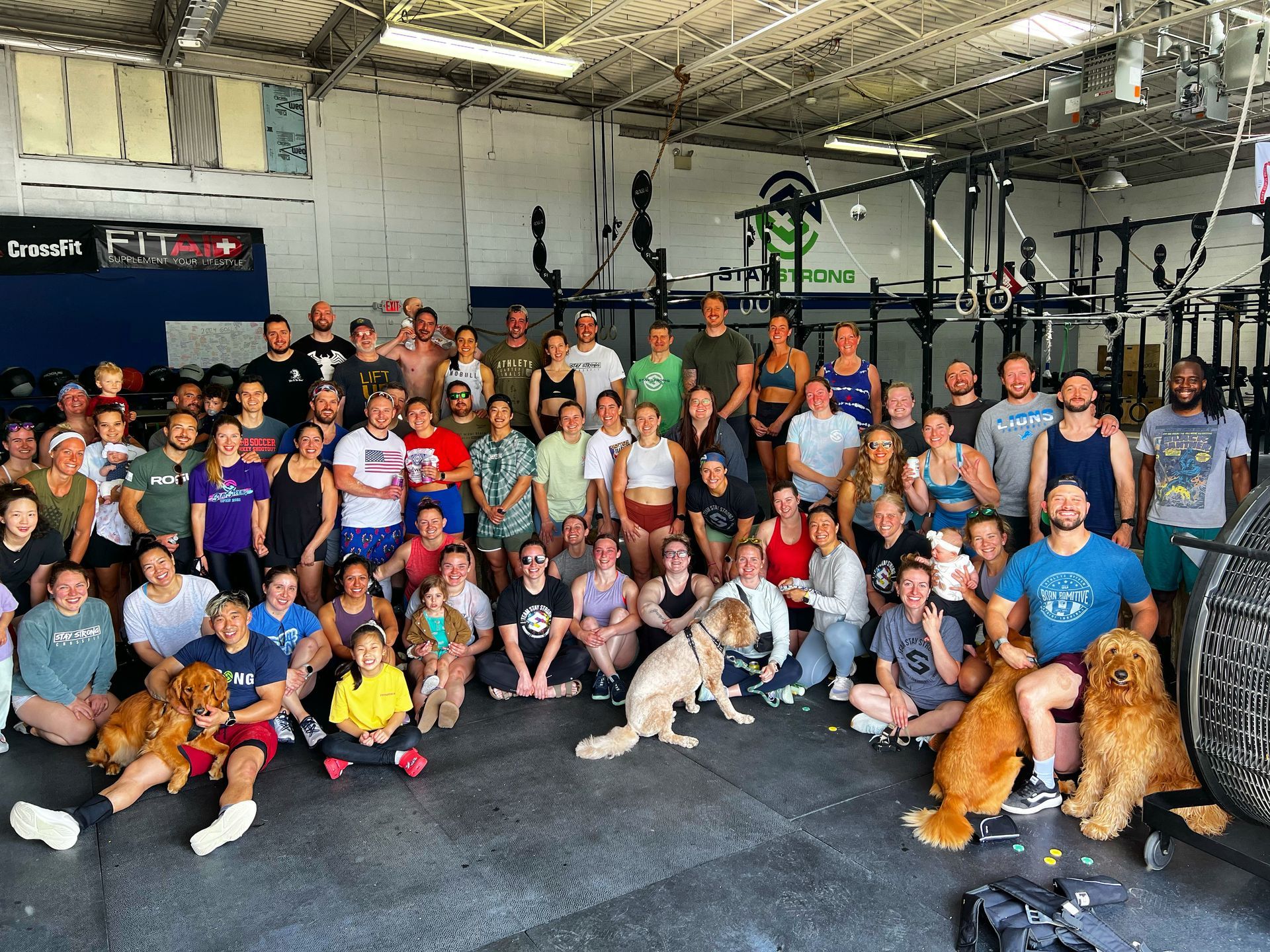 A large group of people and dogs are posing for a picture in a gym.