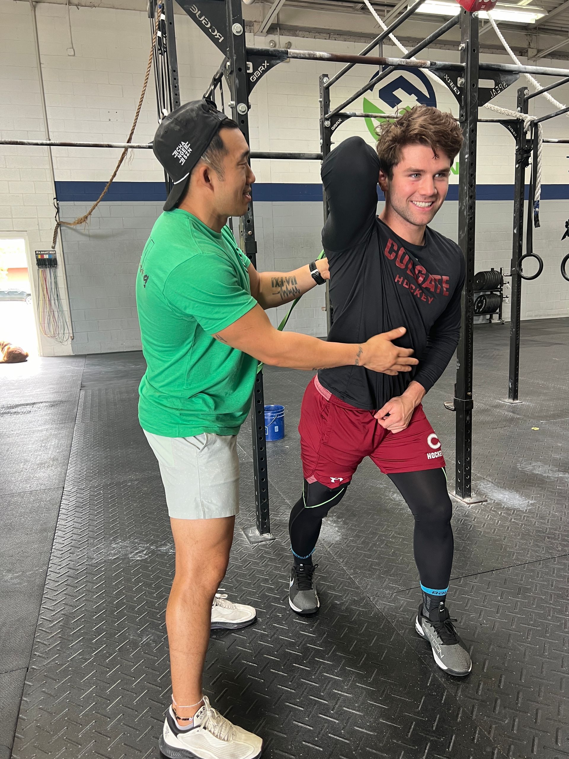 A man is helping another man stretch his arms in a gym.
