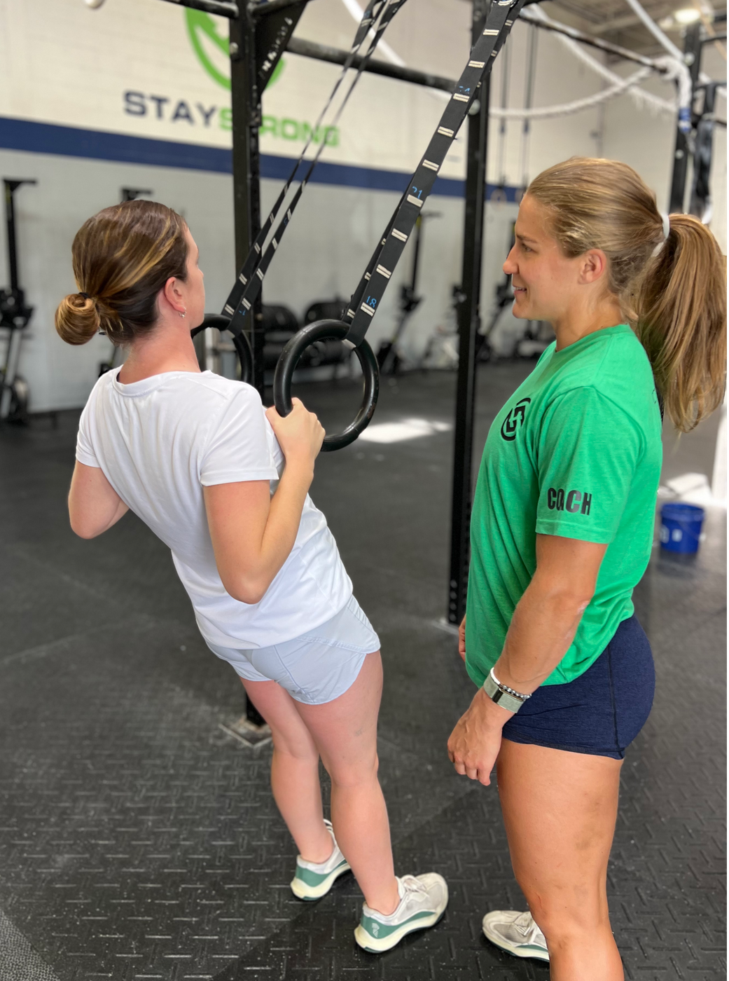 A woman in a green shirt is talking to a woman in a white shirt that while they workout