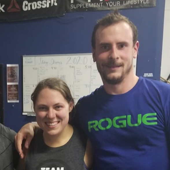 A man and a woman are posing for a picture and the man is wearing a rogue shirt