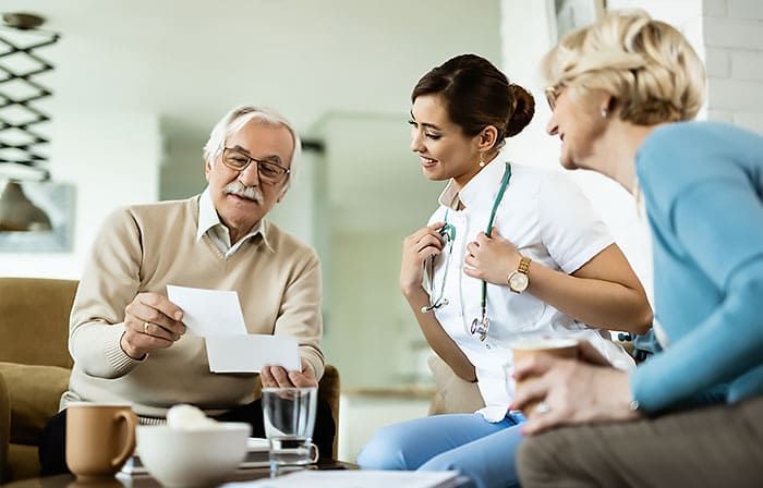 Older woman in wheelchair smiles as a healthcare worker places a hand on her shoulder, looking up.