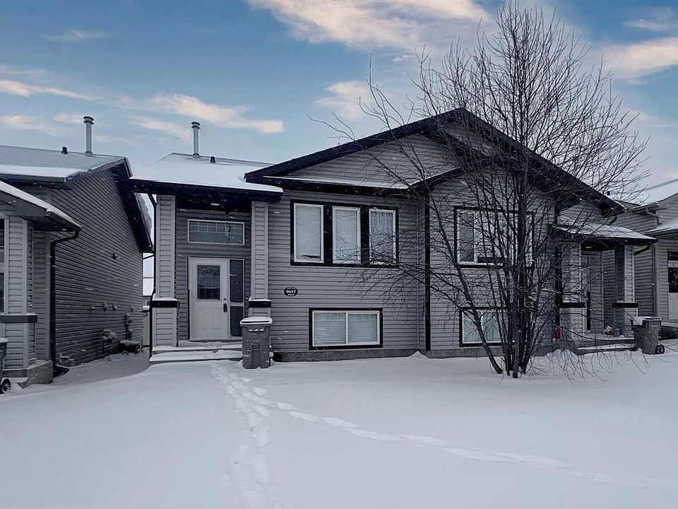 A two-story gray house in winter with snow on the ground and a partly cloudy blue sky.