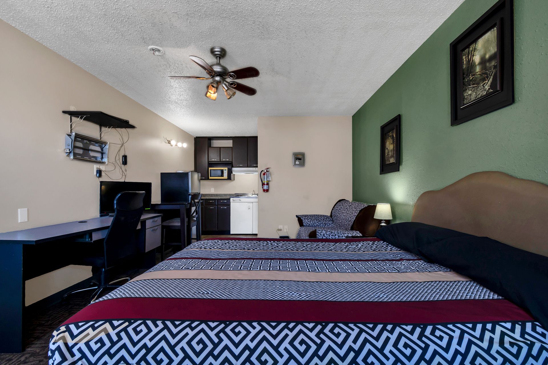 A hotel room with a bed , desk , chair and ceiling fan.