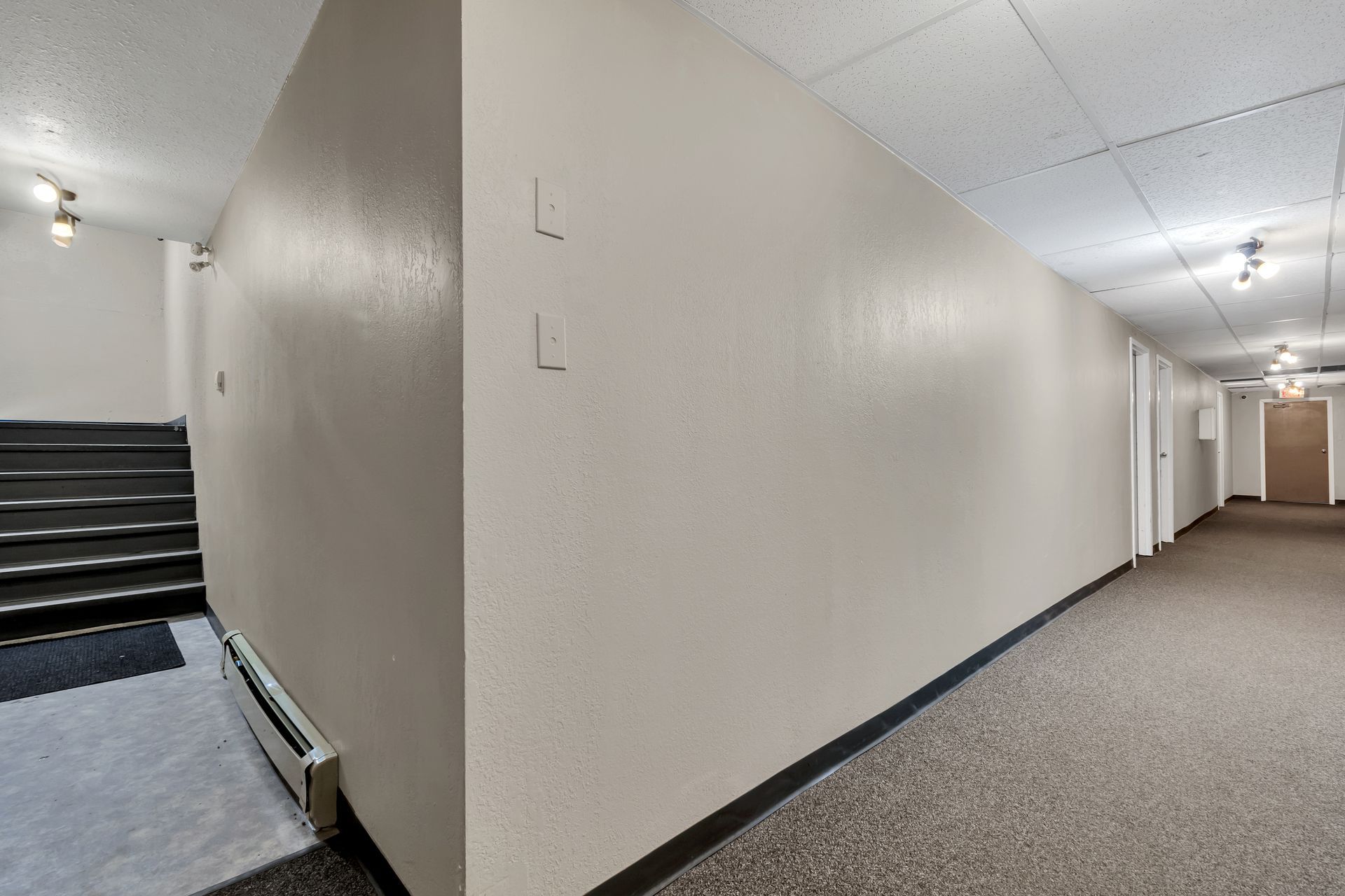 A long hallway with stairs and a carpeted floor in a building.