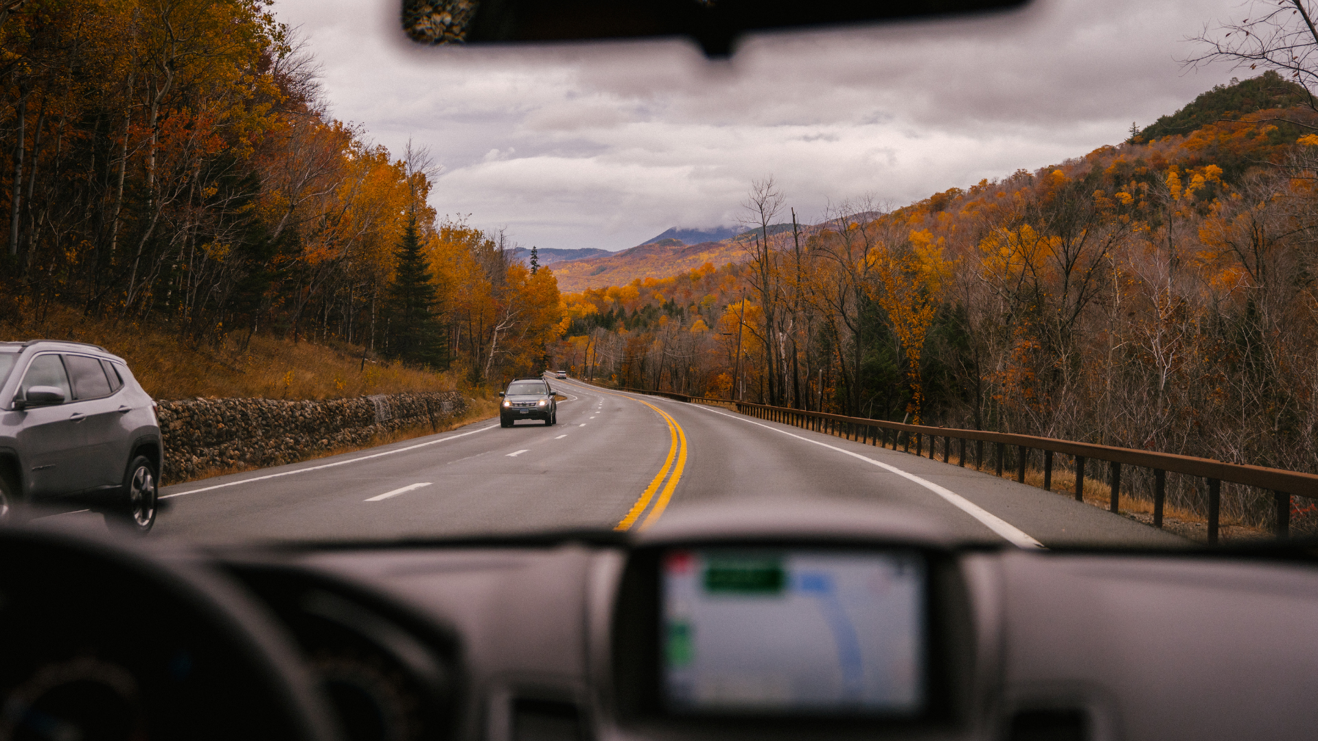 View from car windshield on a winding road through a fall foliage landscape.