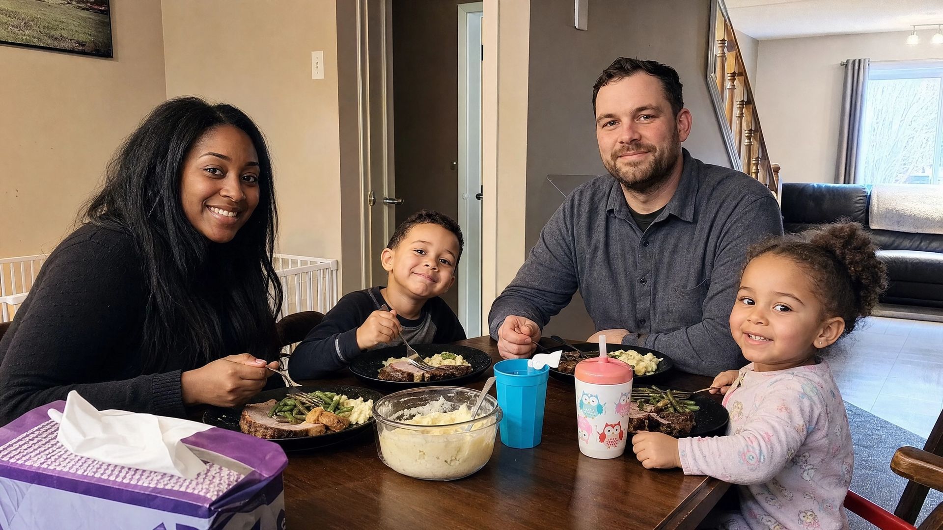 Family gathered around a dining table, smiling and sharing a meal with bowls and cups.