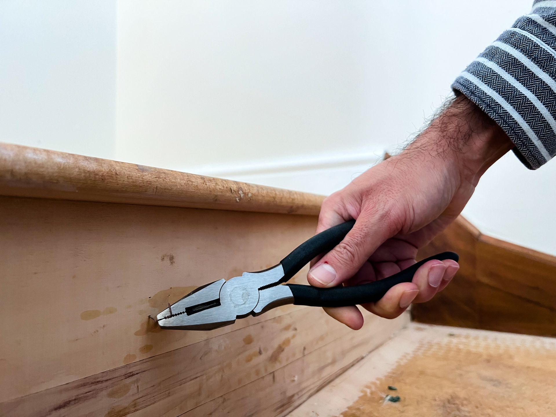 A person is holding a pair of pliers over a piece of wood.
